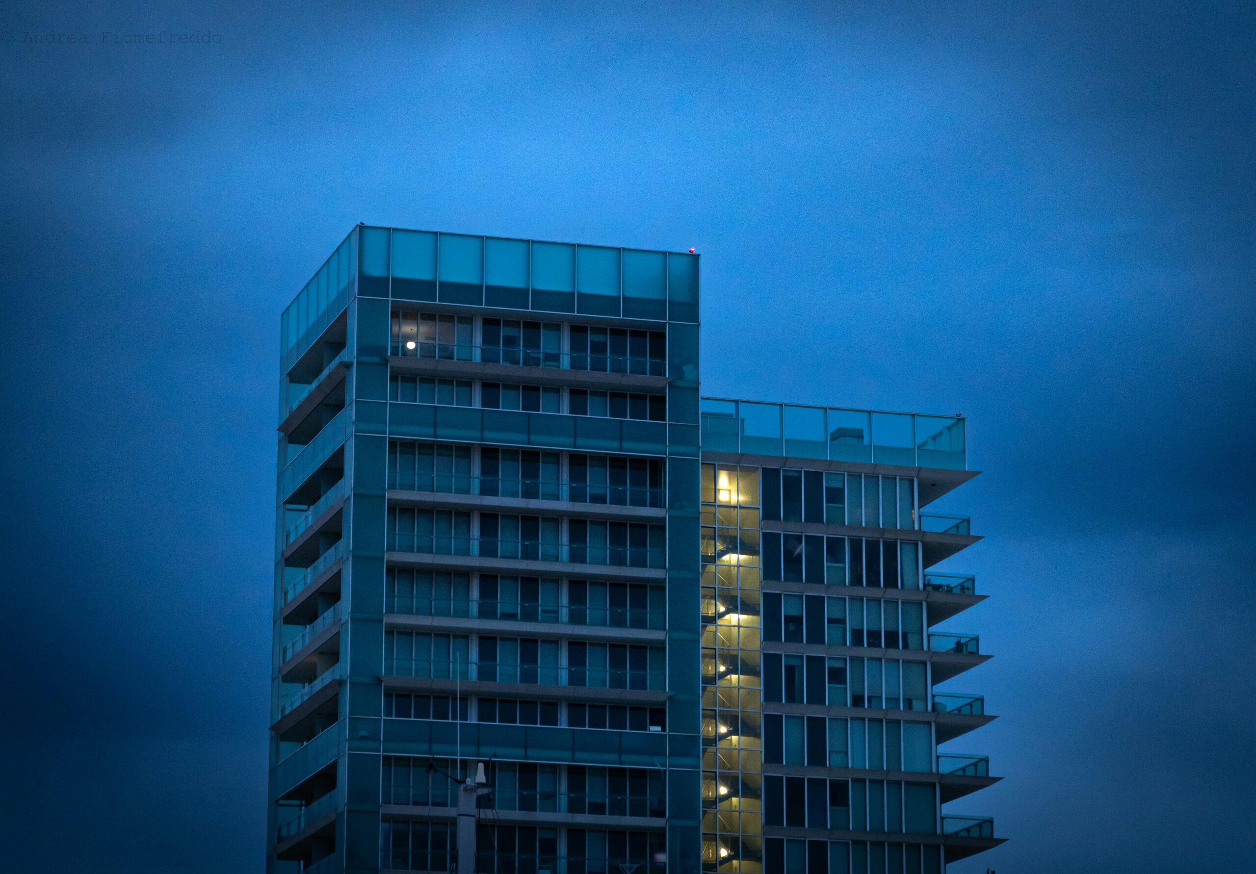 A sleek modern high-rise building with illuminated windows against a moody evening sky.